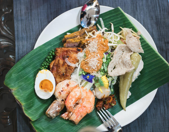 A plate of nasi kerabu with rice, grilled prawns, chicken, vegetables, salted egg and assorted accompaniments on banana leaf.