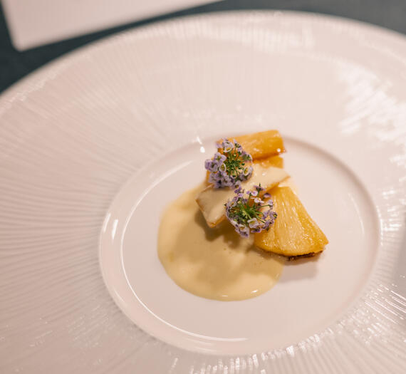 Roasted pineapple with vanilla anglaise and edible flowers on a white plate.